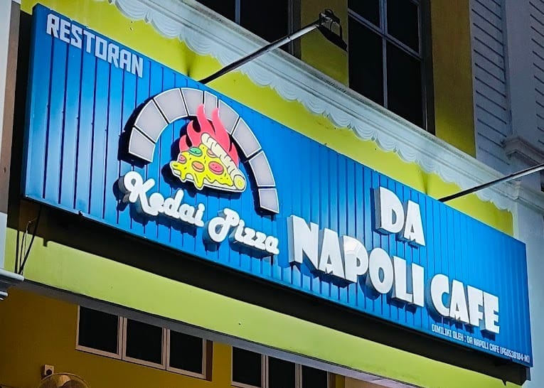 The blue Da Napoli Cafe signboard, reading Restoran, Kedai Pizza, Da Napoli Cafe, lit up at night